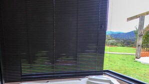 A hot tub with a wooden exterior, positioned indoors with a view of a grassy landscape and mountains through a window. - Chal com Wi-fi e Muito Lazer em Bom Retiro SC (Bom Retiro)
