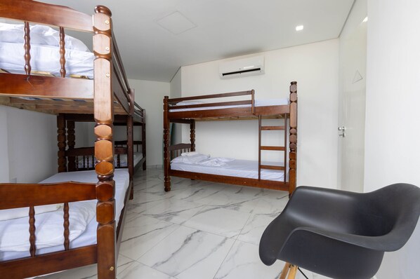 Une pièce avec trois lits superposés, une chaise noire et un appareil de climatisation blanc fixé au mur.