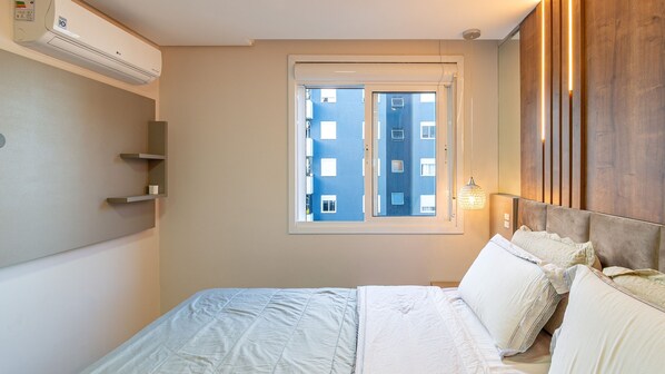 Un dormitorio con cama, ventana y aire acondicionado instalado en la pared.