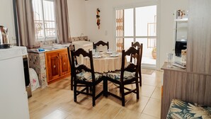 A dining area with a wooden table and chairs, a kitchen with a sink and cabinets, and a view of the outside through large windows. - Timo Apto c Wifi Ar-condicionado e Garagem (Uruguaiana)