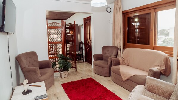 A living room with two brown armchairs, a beige sofa, a red rug, and a wooden partition with a lattice design.