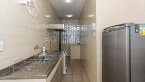 A narrow kitchen with a stainless steel refrigerator, a sink with a drying rack, and a window with a metal grid. - Apto com Wifi e Tima Localiza o Laranjeiras RJ (Rio de Janeiro)