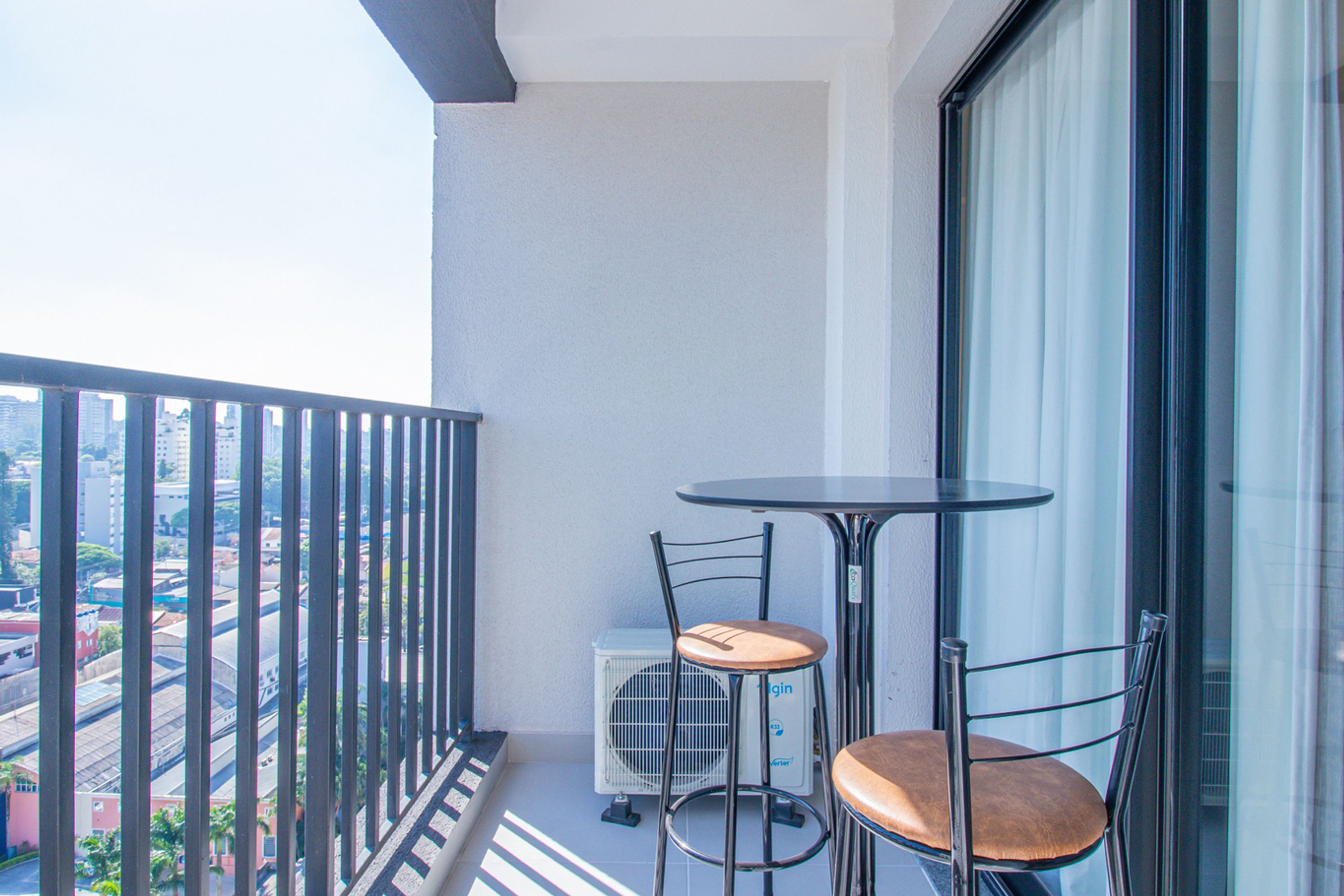 Ein Balkon mit Tisch und zwei Stühlen, ein Fenster und Blick auf eine Stadtansicht.