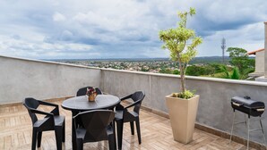 A rooftop terrace with a round table and chairs, a potted plant, and a barbecue grill.