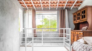 A bedroom with a bed, a wooden cabinet, a window with curtains, and a balcony railing.