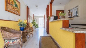 Un hall d’hôtel avec des meubles en osier, un comptoir d’accueil et un grand tableau accroché au mur.