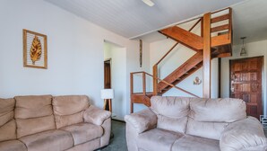 Un salon avec deux canapés beiges, une table basse en verre et un escalier en bois.