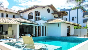 Piscina com borda azulejada, rodeada por um alpendre coberto com cadeiras e uma mesa.