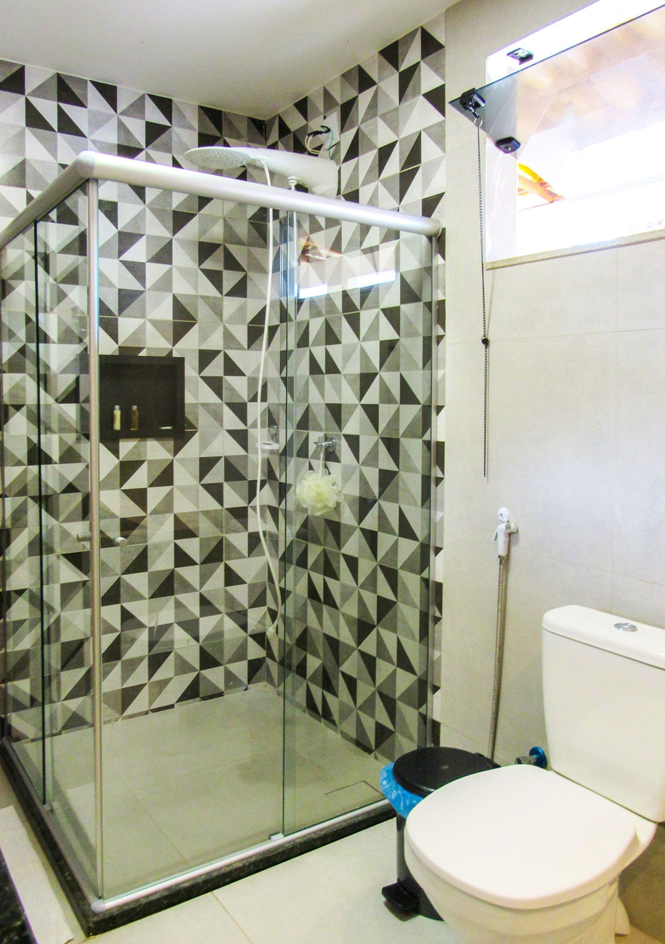 A bathroom with a glass-enclosed shower, a toilet, and a tiled wall with a geometric pattern.