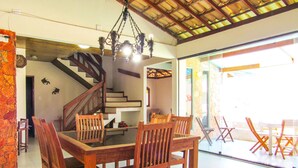 Uma sala de jantar com mesa e cadeiras de madeira, uma escada e vista para o exterior.