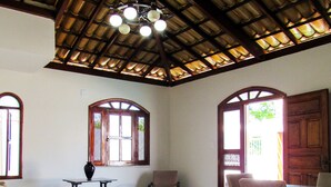 Uma sala de estar espaçosa com teto alto, mesa de jantar com cadeiras, sofá, pequena mesa com um vaso e duas janelas em arco.