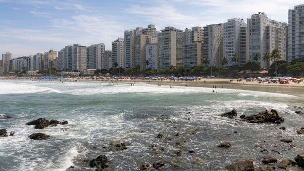 A beach with high-rise buildings in the background, rocky shoreline, and people on the sand. - Apto Top Pitangueiras no Melhor Ponto do Guaruj (Guarujá)