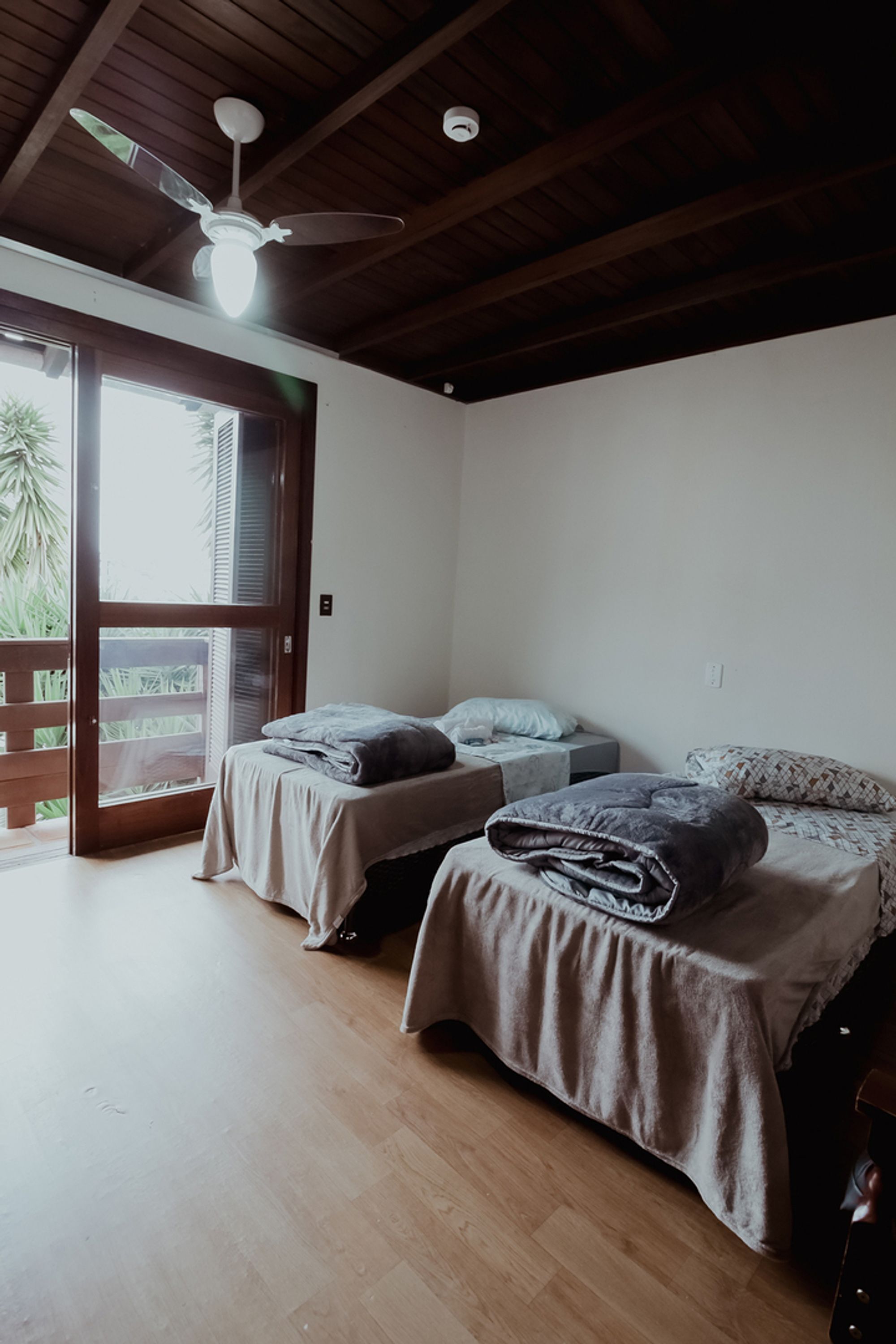 Quarto com duas camas, ventilador de teto e porta de correr para área externa.
