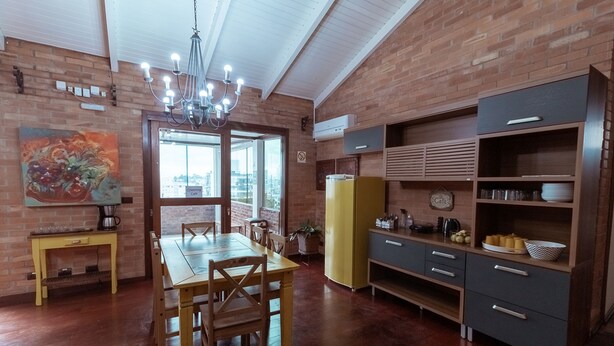 Una cucina con tavolo da pranzo, sedie, un lampadario, un frigorifero e una parete in mattoni.