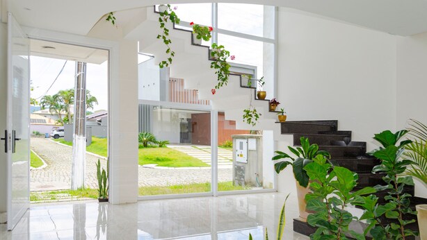 Un interior moderno con un gran ventanal que da a un patio, una escalera y varias plantas en macetas.