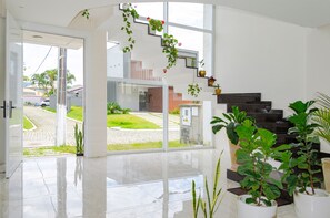 Un intérieur moderne avec une grande porte vitrée donnant sur une cour, un escalier et plusieurs plantes en pot.