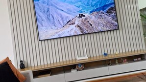 Una sala de estar con un televisor de pantalla plana grande montado en una pared con paneles verticales, una mesa de centro de madera y un sofá con cojines.