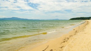 Una playa con agua cristalina, una orilla arenosa y montañas a lo lejos.