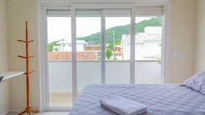 Un dormitorio con una cama, un perchero de madera y vistas a un balcón por un ventanal corredera.