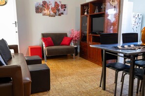 A living room with a sofa, ottoman, and a dining table with chairs. - Apto Confort vel a 170m da Praia Vila Tupi (Praia Grande)