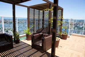 Een balkon met rieten meubilair, plantenbakken en uitzicht op een stadsgezicht.