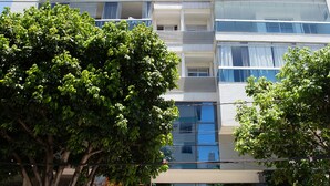 Un edificio a più piani con balconi, un ristorante chiamato "Quitanderia" al piano terra e un albero in primo piano.