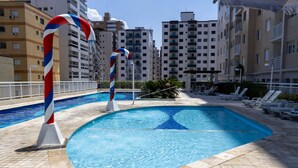 A swimming pool with a unique candy cane design, surrounded by lounge chairs and a tiled deck. - Apto Confort vel a 150m do mar Completo com Lazer (Praia Grande)