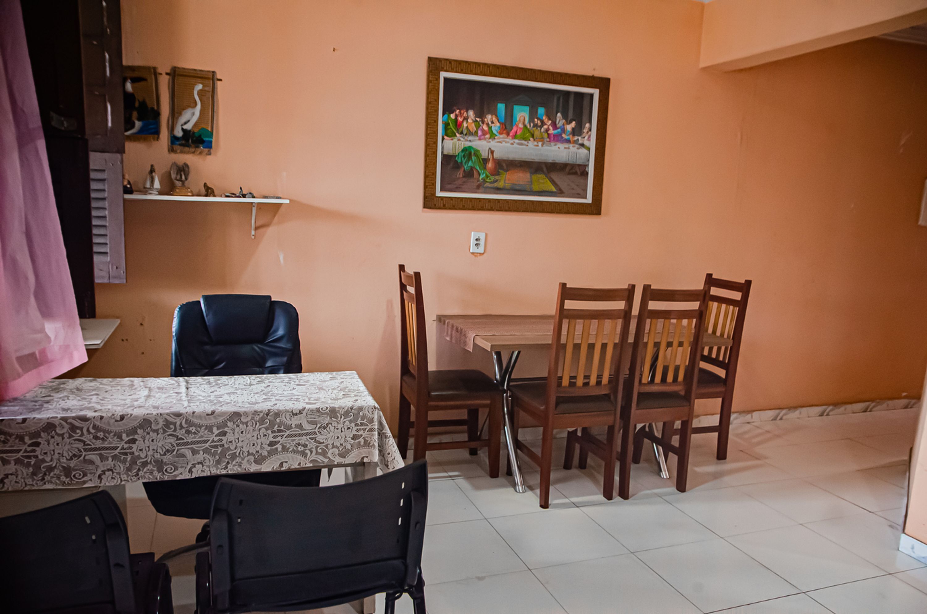 A dining area with a table set for four, wooden chairs, a painting on the wall, and a shelf with decorative items.