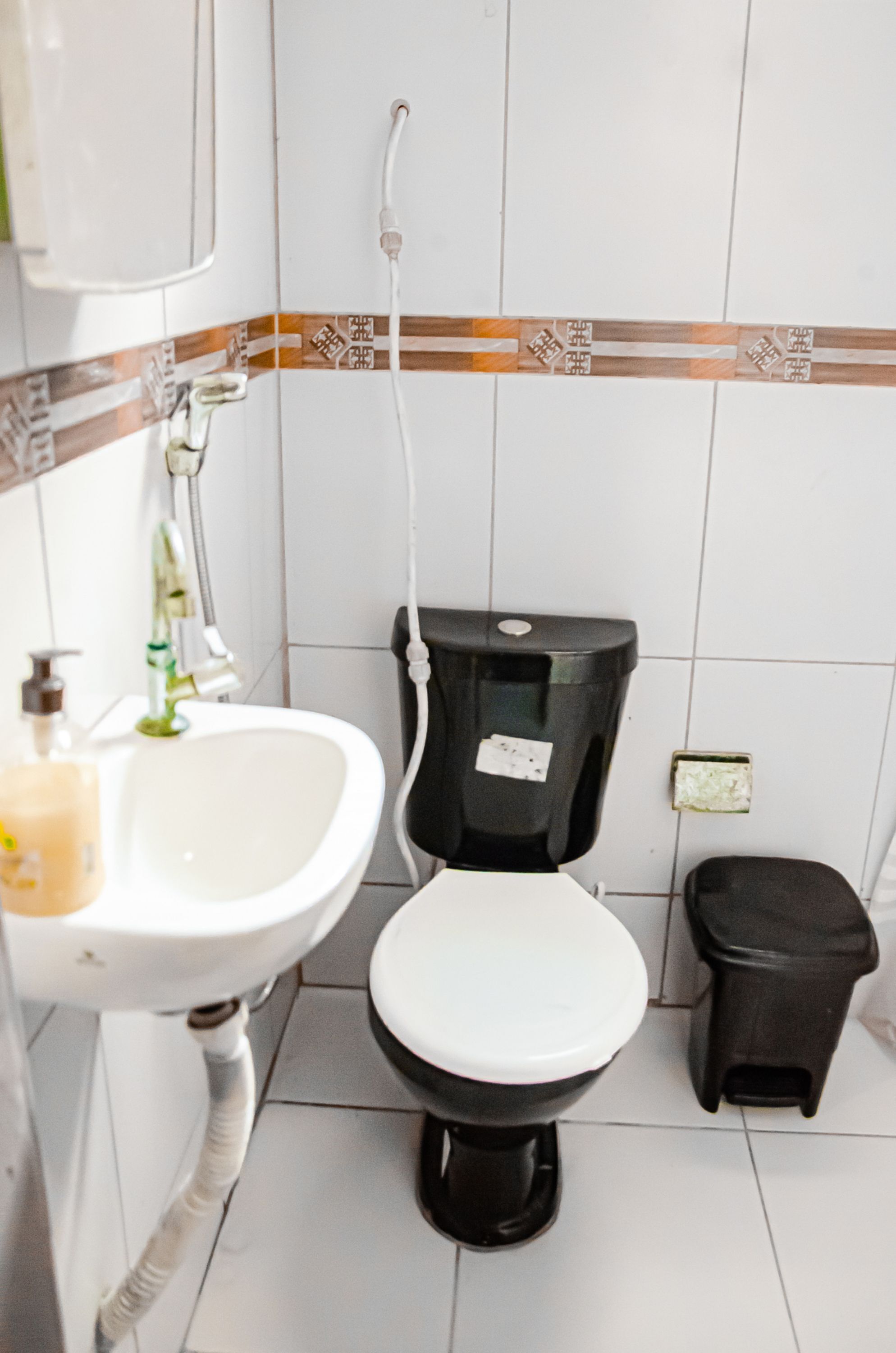 A bathroom with a white sink, black toilet, and a small black trash bin.