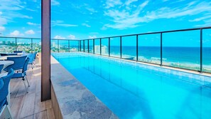 A rooftop infinity pool with a view of the ocean and cityscape.