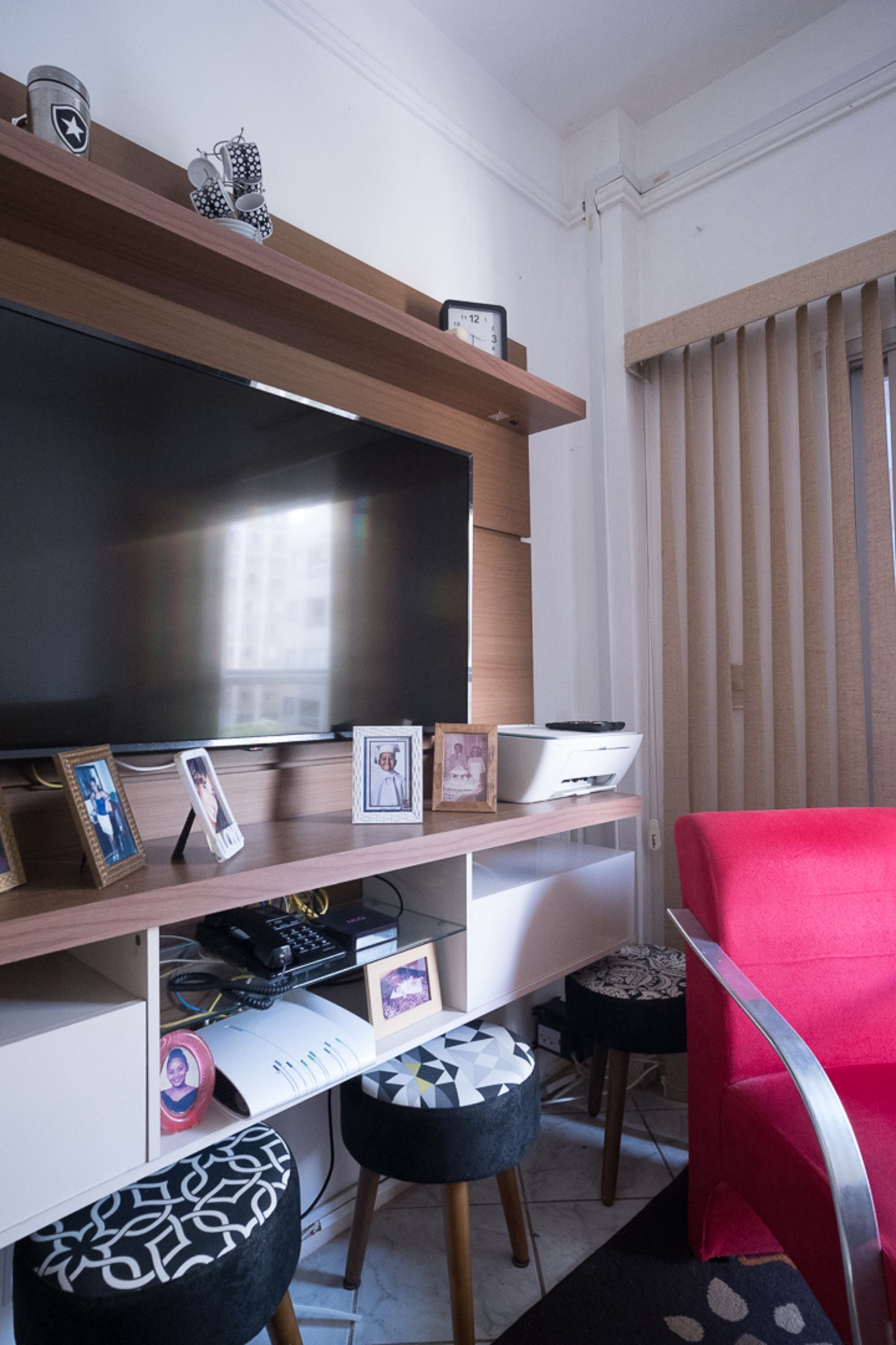 Un salon moderne avec un téléviseur à écran plat, des étagères en bois, des photos encadrées, une imprimante et un fauteuil rouge.