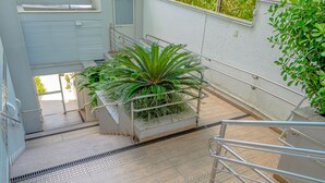 A staircase with metal railings, a potted plant, and a tiled floor with tactile paving for visually impaired individuals. - Apartamento Completo em Trindade Perto da Ufsc (Florianópolis)