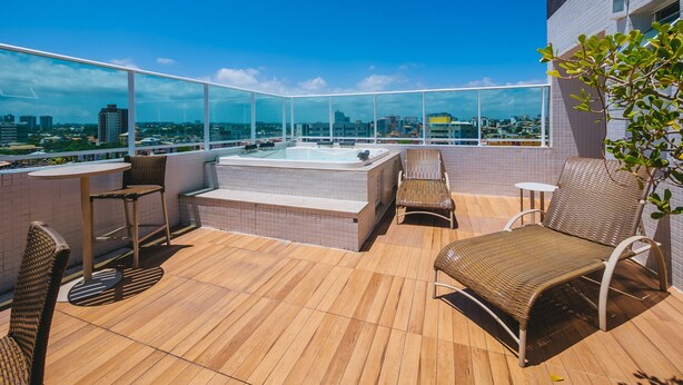 Eine Dachterrasse mit Whirlpool, Korbstühlen und Blick auf die Stadt.