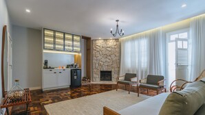 Una sala moderna con chimenea, piso de madera, un sofá y una zona de cocina con pared de piedra y armarios empotrados.