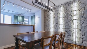 Un comedor con una mesa y sillas de madera, una pared de piedra y una cocina al fondo.