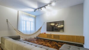 Una sala de estar moderna con un amplio sofá modular, una hamaca, un televisor de pantalla plana y suelo de madera.