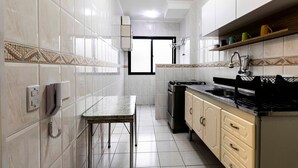 A narrow kitchen with white tiled walls, a built-in stove, and a small dining table.