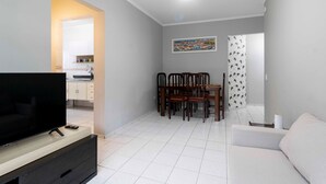 A modern living room with a flat-screen TV, a dining area with wooden chairs and a table, and a white sofa.