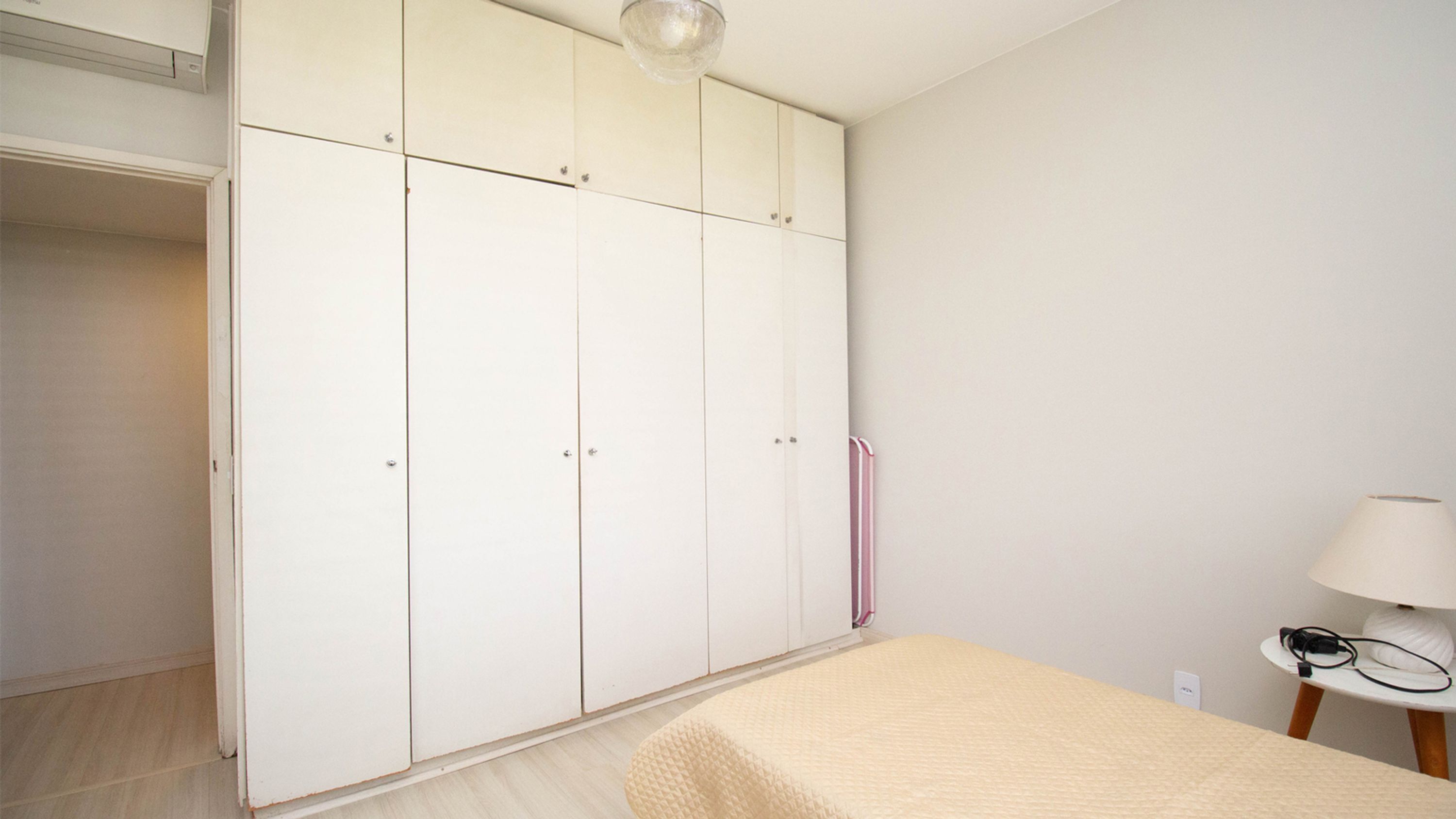 A bedroom with a bed, a wardrobe, and a bedside table with a lamp.
