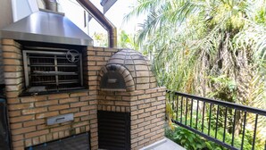 A brick-built outdoor kitchen with a chimney and a grill, surrounded by lush greenery. - Casa em Condom nio com Piscina Wi-fi e Garagem (Guarujá)