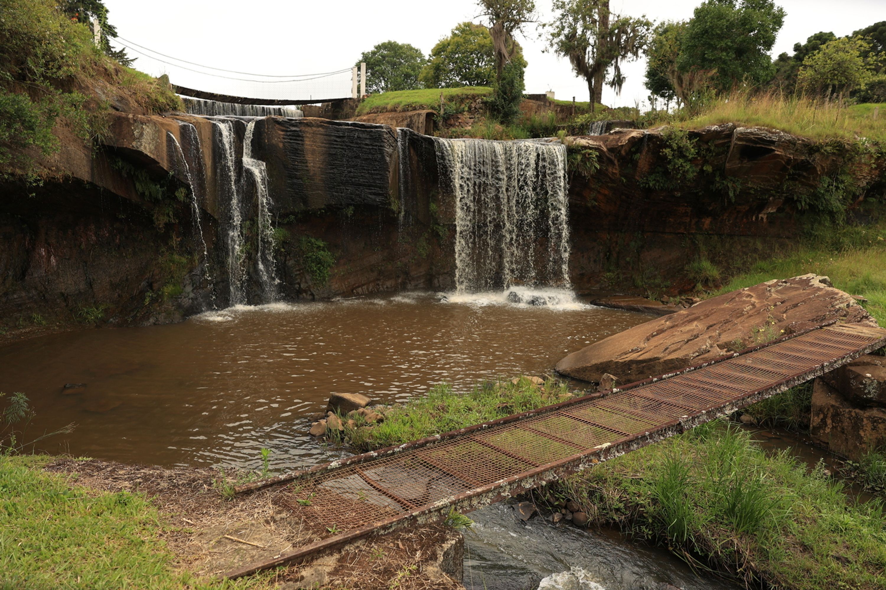 Una cascada natural con un puente metálico cruzando un río.