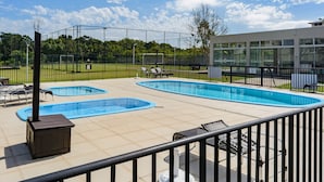 A rooftop pool area with two swimming pools, lounge chairs, and a building in the background. - Apto c Tima Localiza o Prox Praias e pq Aquatico (Florianópolis)