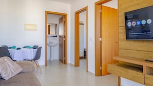 A modern living room with a TV, a dining area with a table and chairs, and a kitchen area with a sink. - Apto c Tima Localiza o Prox Praias e pq Aquatico (Florianópolis)