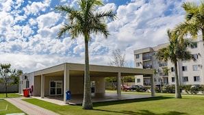 A modern building with a covered outdoor area, palm trees, and a clear sky. - Apto c Tima Localiza o Prox Praias e pq Aquatico (Florianópolis)