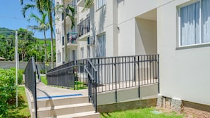 A residential building with a staircase leading to a balcony, surrounded by greenery and a clear sky. - Apto c Tima Localiza o Prox Praias e pq Aquatico (Florianópolis)