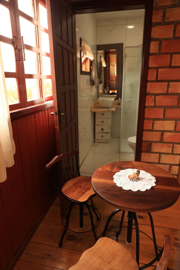Un coin repas en bois avec une table et des chaises, un petit tabouret et un chemin de table en dentelle posé sur la table.