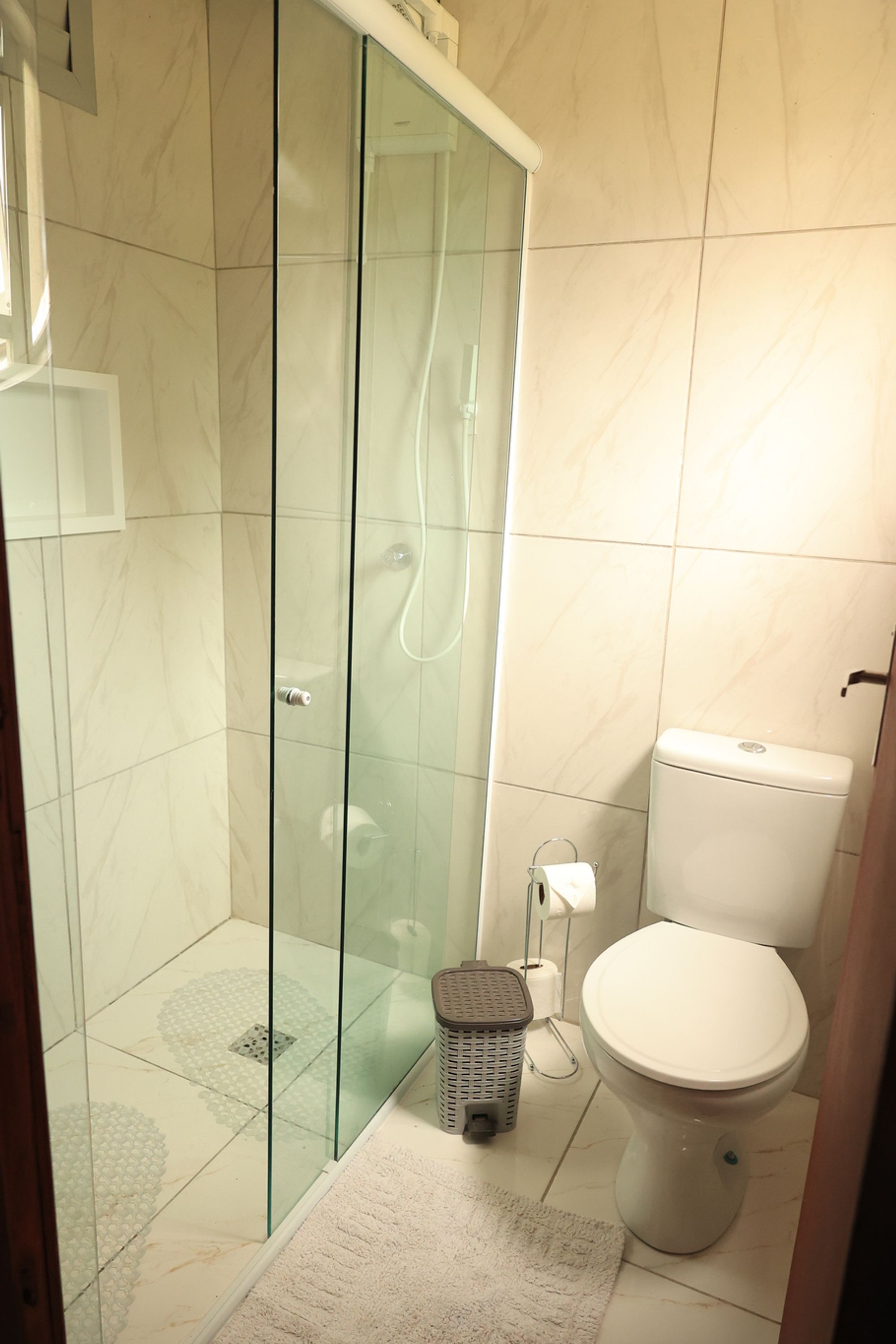 Un baño con cabina de ducha de vidrio, un inodoro y un pequeño cubo de basura.