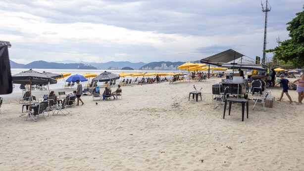 A beach with umbrellas, chairs, and a food cart. - Apto Confort vel com Linda Vista Frente Para o mar (Santos)