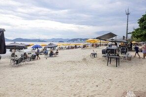 A beach with umbrellas, chairs, and a food cart. - Apto Confort vel com Linda Vista Frente Para o mar (Santos)