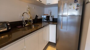 A modern kitchen with a stainless steel refrigerator, a microwave, a toaster, and a sink. - Apto Confort vel com Linda Vista Frente Para o mar (Santos)